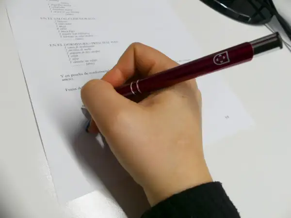 Mano con bolígrafo revisando un inventario de muebles para un contrato de alquiler, cumpliendo la ley de arrendamientos urbanos.
