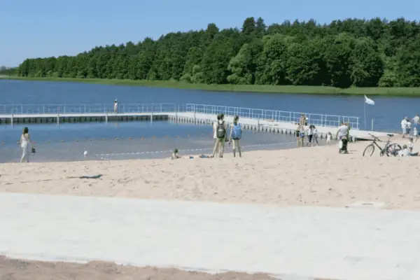 Słoneczne plaże na Mazurach przyciągają ludzi. Dzieci bawią się na piasku, a dorośli spacerują po pomoście.