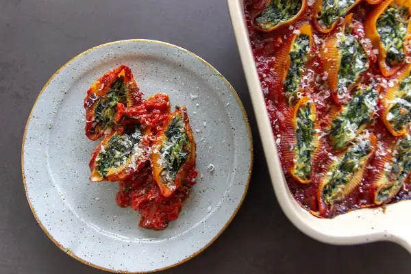 Gevulde pasta schelpen met spinazie en tomatensaus, een heerlijk voorbeeld van wat vega eten kan zijn.
