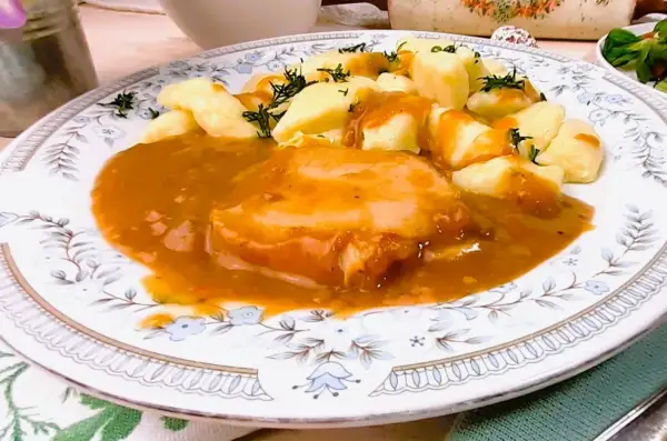 Pyszny schab w sosie, podany z kluskami śląskimi i posypany koperkiem. Danie prezentuje się apetycznie na ozdobnym talerzu.