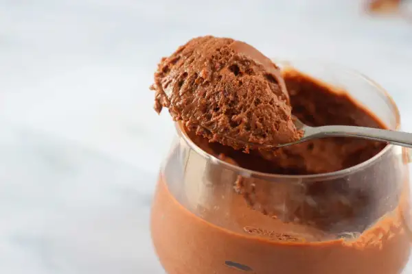 Un cucchiaio raccoglie una porzione generosa di soffice mousse al cioccolato da un bicchiere trasparente.