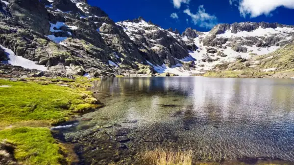 Espectacular vista de la ruta laguna grande de Gredos, con montañas nevadas, césped verde y aguas cristalinas.