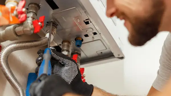 Tecnico con guanti lavora su caldaia Baxi in blocco, cercando di sbloccarla con un cacciavite.