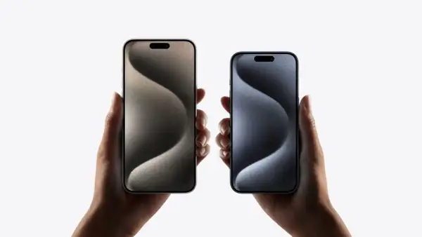 Dwie dłonie trzymają iPhone'y 15 w różnych kolorach. Zastanawiasz się nad ich **pojemnością baterii**?