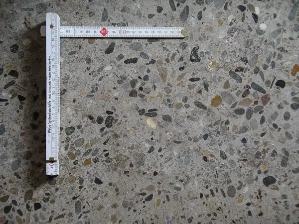 Superficie di calcestruzzo a vista con aggregati di varie dimensioni. Un righello pieghevole misura la **classe di esposizione calcestruzzo**.