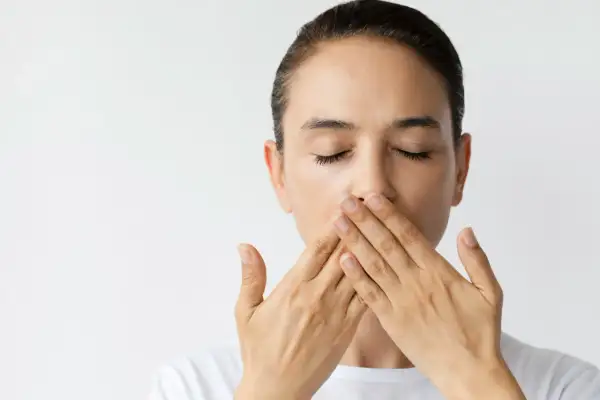 Donna con occhi chiusi copre la bocca con le mani, un'espressione che suggerisce una bocca amara o un segreto.