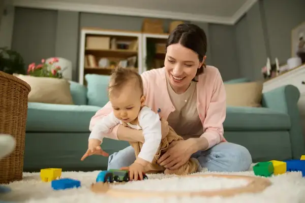 Mama bawi się z dzieckiem na dywanie, budując tory dla pociągu. To czas na zabawę i rozwijanie umiejętności, czyli aktywnie w pracy nad rozwojem malucha.
