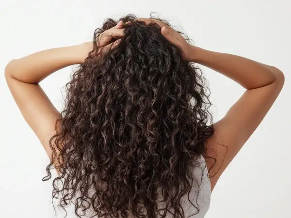 Vista trasera de una persona con un hermoso pelo rizado oscuro, sus manos acarician su melena.