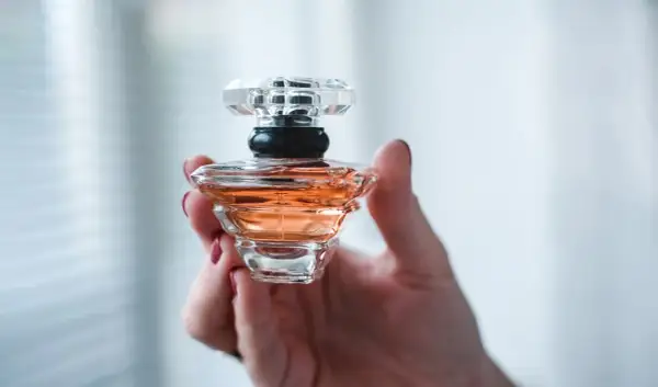 Dłoń trzyma flakonik perfum o bursztynowym kolorze. Wygląda jak dzieło sztuki, może to baccarat kurkdjian?