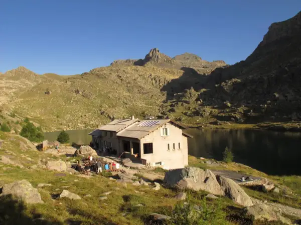 Refuge de montagne au bord d'un lac, idéal pour une randonnée vallée des merveilles 2 jours. Des randonneurs se reposent.
