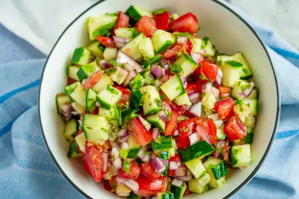 Frischer Tomaten-Gurken-Salat mit roten Zwiebeln und Kräutern, serviert in einer Schüssel.