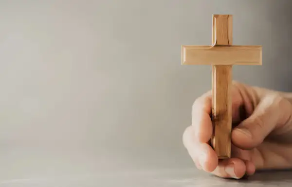 Eine Hand hält ein hölzernes Kreuz, ein Symbol, das Christen weltweit verbindet.