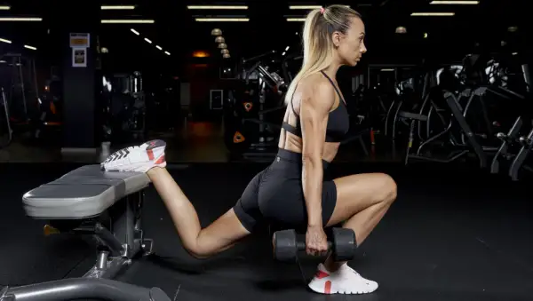 Donna esegue affondi bulgari con manubrio, concentrandosi sull'allenamento dei glutei e sull'iperestensione.