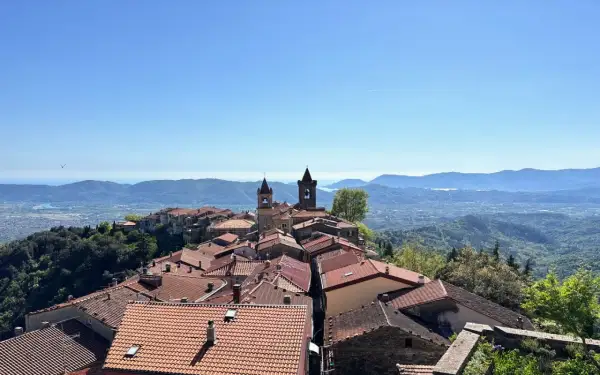 Panoramica di un borgo collinare con tetti rossi e campanili, che rivela dove si trova Fosdinovo, con il mare e le montagne all'orizzonte.