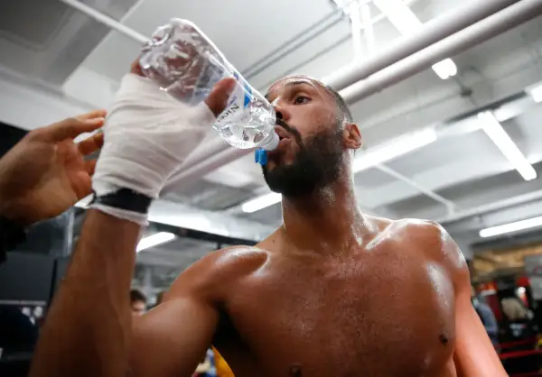 A boxer, hand-wrapped, drinks from a water bottle. This shows why boxers spit out water: to stay hydrated without swallowing too much.
