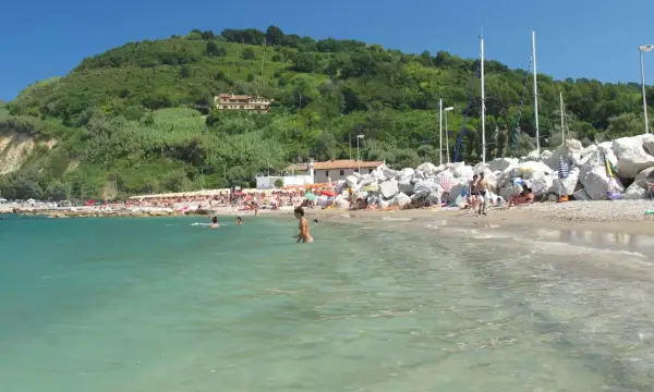 Spiaggia affollata a Gabicce Mare, con gente che nuota e prende il sole sotto un cielo azzurro.
