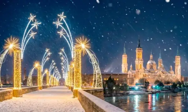 Puente nevado con encendido luces navidad Zaragoza. La Basílica del Pilar brilla bajo la nieve.