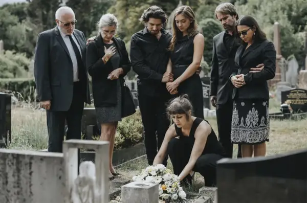 Trauernde Familie in schwarzer Beerdigungskleidung legt Blumen nieder.