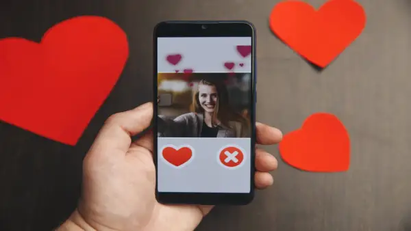 Dłoń trzyma smartfon z profilem kobiety, obok czerwone serca. To może być początek poszukiwań na najpopularniejsze portale randkowe w Polsce.
