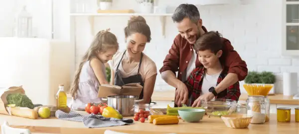 Famille préparant un repas. Le père aide son fils à couper des légumes. La mère et la fille consultent un livre de recettes. On se demande : lactose c'est quoi ?