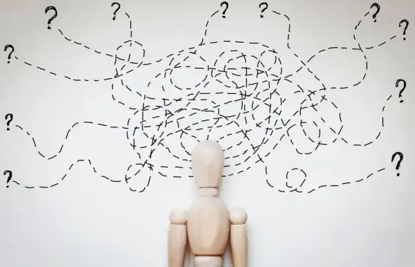 Drewniany manekin z chaotycznymi liniami i znakami zapytania nad głową, symbolizującymi trudności w diagnozie, np. borderline ICD 10.