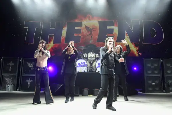 Członkowie Black Sabbath na scenie podczas koncertu "The End". Ozzy Osbourne z mikrofonem, pozostali członkowie klaszczą.