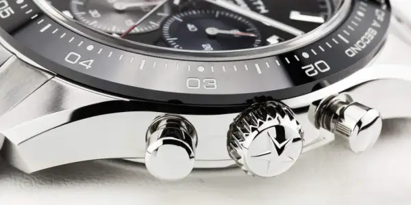Detalle de un reloj de lujo, mostrando el bisel con números y marcas, y los pulsadores. El bisel del reloj está diseñado para cambiar la hora.