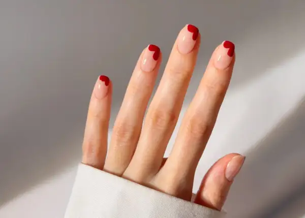 Une main aux ongles nude ornés de petits cœurs rouges. Une idée ongle coeur parfaite pour la Saint-Valentin ou pour ajouter une touche d'amour à votre quotidien.