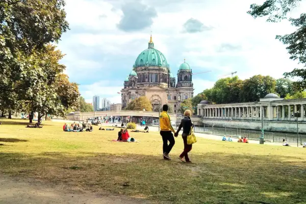 Ett par promenerar på en gräsmatta med Berlin domkyrka i bakgrunden. Många njuter av solskenet, en perfekt dag för aktiviteter i Berlin.
