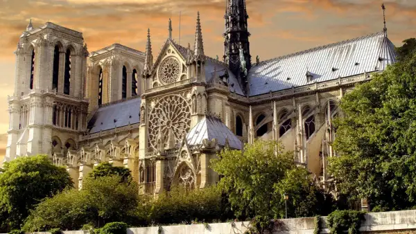 Katedra Notre Dame w Paryżu z różanymi oknami i wieżami na tle pomarańczowego nieba.