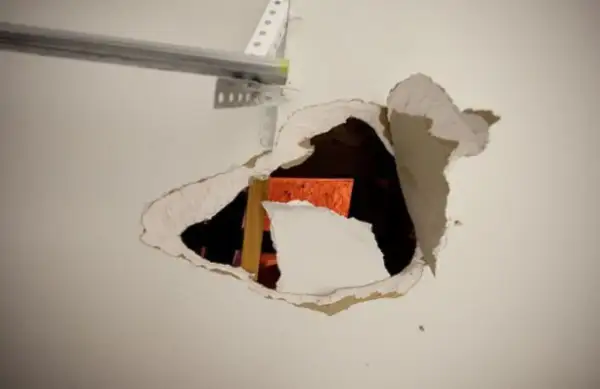 Un **buco nel muro troppo grande** rivela una struttura arancione e un montante di legno.