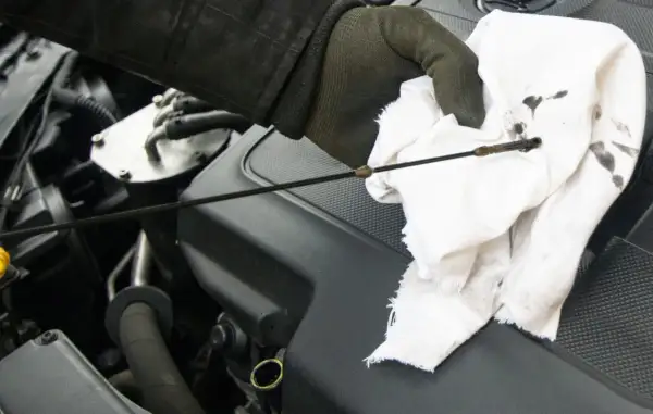 Sprawdzanie poziomu oleju w silniku fiat stilo 1.9 jtd. Ręka w rękawiczce wyciera bagnet.