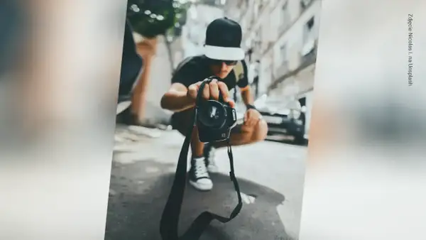 Młody fotograf w czapce z daszkiem trzyma aparat, gotowy do uchwycenia chwili. Zastanawiasz się, ile zarabia fotograf?