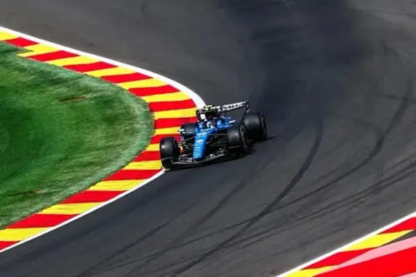 Un coche azul de Fórmula 1 toma una curva cerrada en la pista, con la hierba y las rayas rojas y amarillas de la escapatoria a su lado. La clasificación de Fórmula 1 hoy promete emoción.