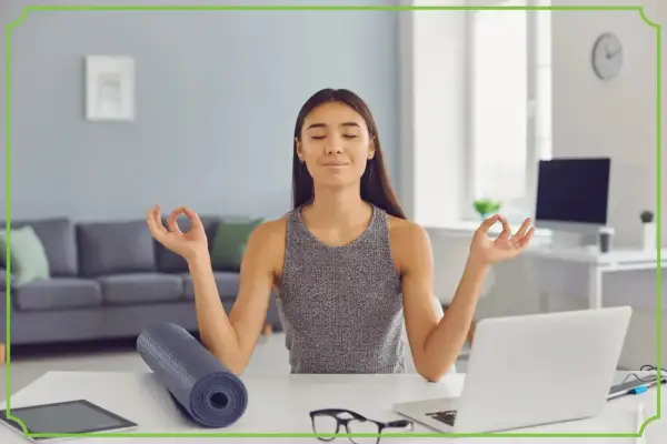Kobieta medytuje przy biurku, osiągając work life balance. Obok leży mata do jogi i laptop.