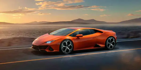 Pomarańczowy Lamborghini Huracan Evo pędzi wzdłuż malowniczego wybrzeża o zachodzie słońca.