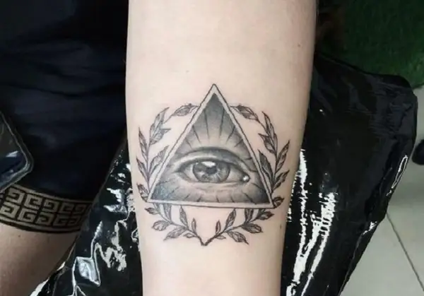 Oko proroka tatuaz w trójkącie otoczone gałązkami. Symbol czujności i wiedzy.