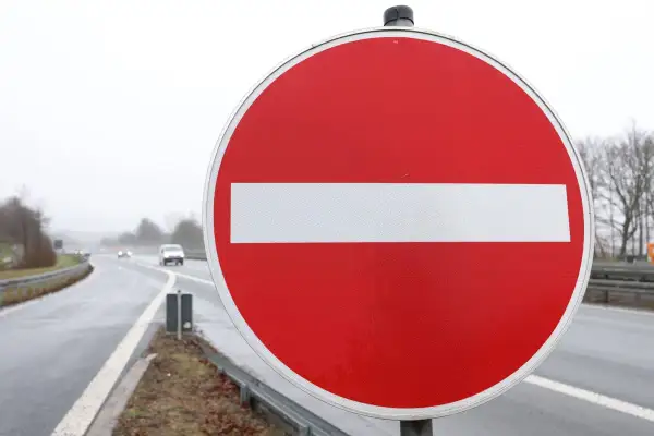 Ein rotes Rundschild mit weißem Balken: durchfahrt verboten schild. Autos fahren auf nasser Straße im Hintergrund.