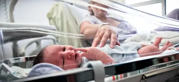 Noworodek, dziecko urodzone w 36 tygodniu, leży w inkubatorze. Mama delikatnie dotyka jego paluszka.