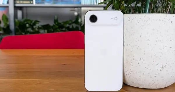 Biały iPhone 5c z charakterystycznym modułem aparatu, stojący na drewnianym blacie obok doniczki.