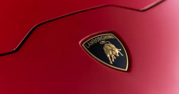 Złote logo Lamborghini z bykiem na czerwonym tle, symbol luksusowych marek samochodów.