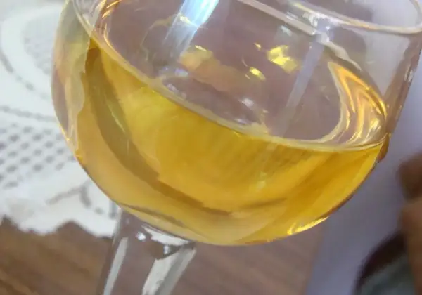 Złocisty płyn w kieliszku, być może aromatyczne wino mandarynkowe, odbija światło.