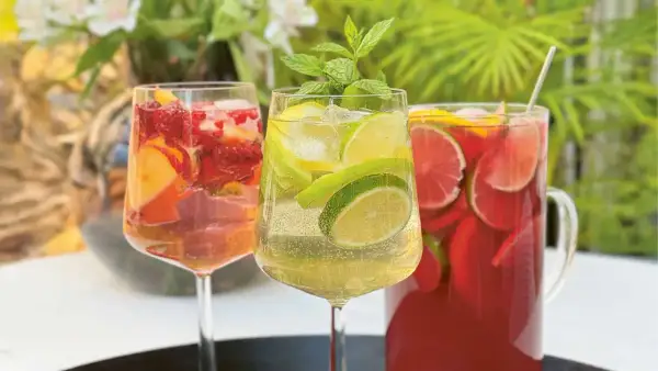 Tre glas med alkoholfri sangria fyllda med frukt och is. En kanna med röd sangria i bakgrunden.