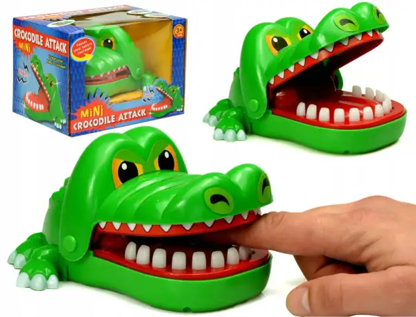 Zielona zabawka gra krokodyl z otwartą paszczą, do której włożono palec. Obok pudełko z napisem "Mini Crocodile Attack".