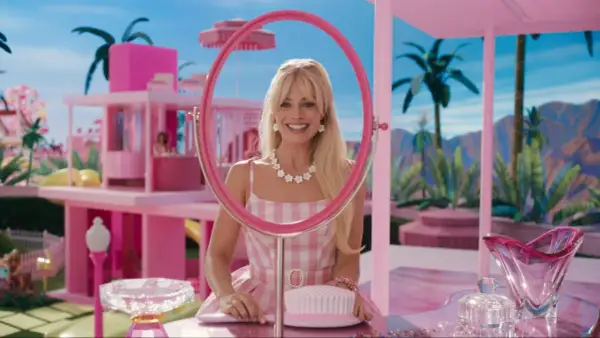 Margot Robbie als Barbie in ihrem pinken Traumhaus, lächelnd durch einen Spiegel.