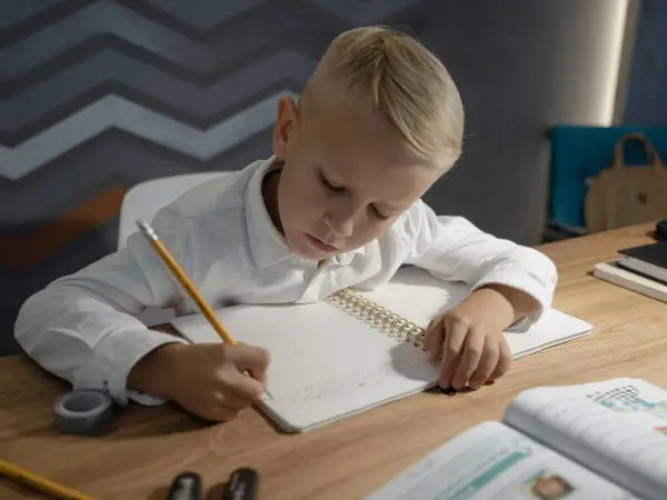 Niño rubio concentrado escribiendo en su cuaderno, practicando el dictado 4 primaria.