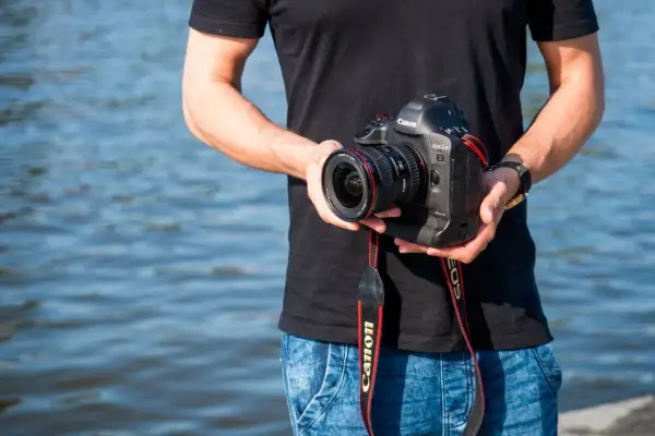 Mężczyzna trzyma aparat Canon EOS-1D Mark II z obiektywem, idealny do fotografii krajobrazowej dzięki matrycy APS-C.