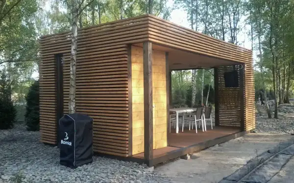 Nowoczesna altana z drewna, idealna na letnie spotkania. W środku stół z krzesłami, gotowa na przyjęcie gości.