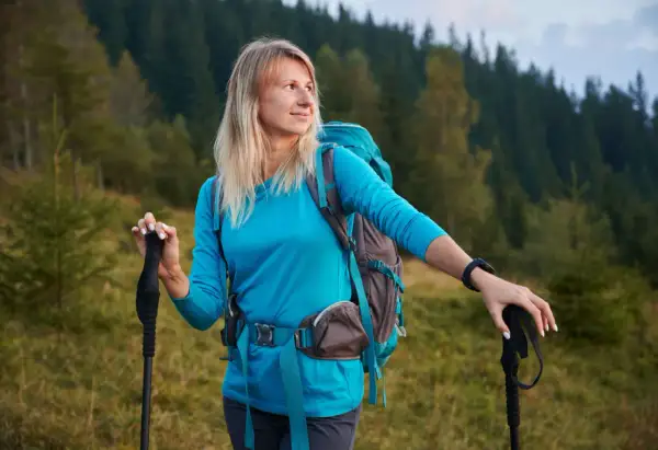 Frau mit Rucksack und Wanderstöcken in den Bergen. Wandern ist eine tolle Aktivität für den Kalorienverbrauch.