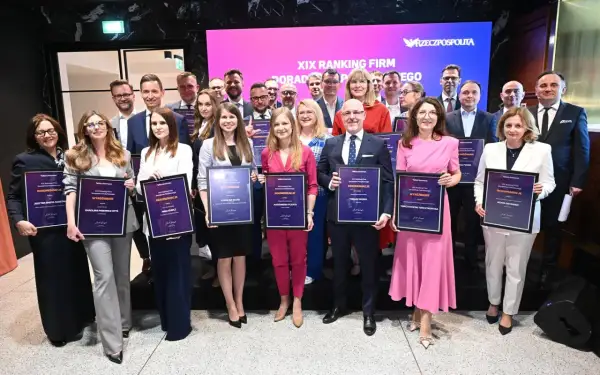 Grupa ludzi w eleganckich strojach pozuje do zdjęcia z dyplomami w rękach na tle ekranu z napisem "XIX Ranking Firm Doradztwa Podatkowego".